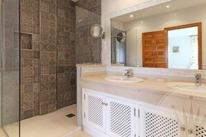 Une salle de bain avec des carreaux décorés, un grand miroir, un lavabo double et une porte en bois.