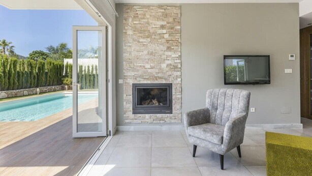 Una sala de estar moderna con chimenea de piedra, un sillón cómodo y un televisor montado en la pared.