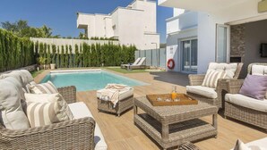 Un área de piscina moderna al aire libre con mobiliario de mimbre, una mesa de vidrio y vista despejada a la piscina.