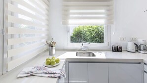 Una cocina moderna con ventana, pileta de acero inoxidable y muebles de cocina blancos.