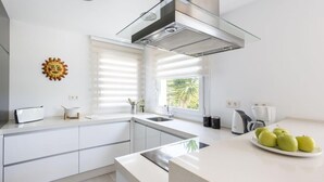 Una cocina moderna con armarios blancos, una campana extractora de acero inoxidable, una ventana con persianas y un plato de manzanas verdes sobre la encimera.