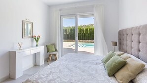 Un dormitorio con cama, escritorio, silla y vista a una piscina.