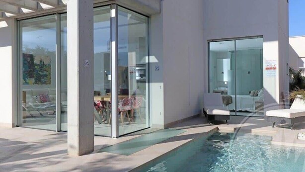 A modern building with a glass facade, a pool area with lounge chairs, and a clear view of the surrounding landscape. - La Manga Club Las Dalias Villa 564 (La Manga Club, Cartagena)