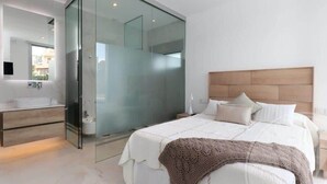 A modern bedroom with a glass shower enclosure, a wooden headboard, and a bedside table with a lamp. - La Manga Club Las Dalias Villa 564 (La Manga Club, Cartagena)