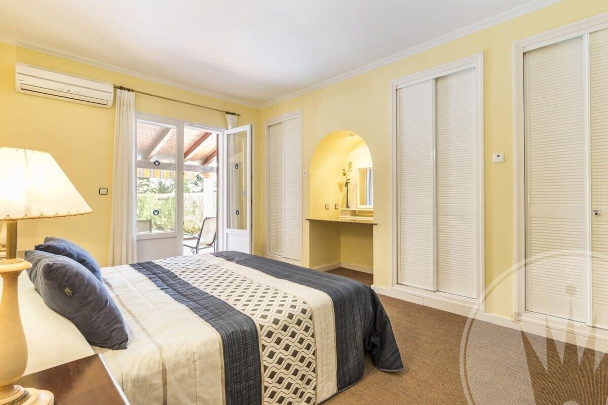 A bedroom with a bed, a bedside table with a lamp, a mirror, and a sliding door leading to a balcony.