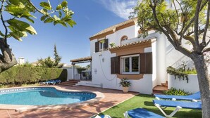 A poolside area with a swimming pool, sun loungers, and a white building with brown trim and shutters. - La Manga Club Las Brisas Villa 514 (La Manga Club, Cartagena)
