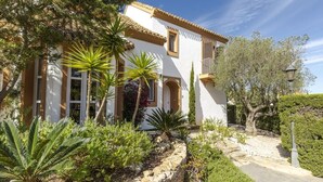 A Mediterranean-style villa with a white facade, terracotta roof tiles, and a stone pathway leading to the entrance. - La Manga Club Las Brisas Villa 514 (La Manga Club, Cartagena)