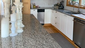 A kitchen with granite countertops, white cabinets, a stainless steel dishwasher, and a window with a view of greenery. - Exclusive walk to the beach Lazy Point House (Amagansett)