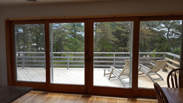 A room with large sliding glass doors leading to an outdoor deck with wooden railings and two Adirondack chairs. - Exclusive walk to the beach Lazy Point House (Amagansett)
