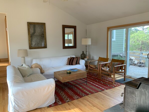 A living room with a white sofa, two armchairs, a coffee table, and a fireplace. There is a large window with a view of the outdoors. - Exclusive walk to the beach Lazy Point House (Amagansett)