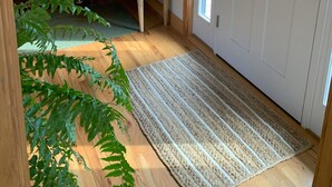 A wooden bench with a patterned cushion, a wall-mounted mirror, a door with a window, and a doormat. - Exclusive walk to the beach Lazy Point House (Amagansett)