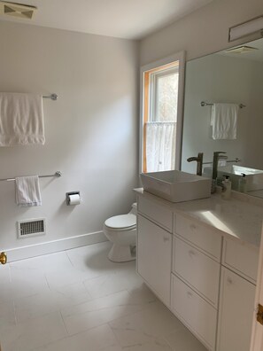 A modern bathroom with a white sink, vanity, and toilet. There is a window providing natural light and a towel rack on the wall. - Exclusive walk to the beach Lazy Point House (Amagansett)
