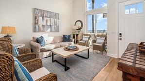 A spacious living room with a beige sofa, wicker chairs, a coffee table, and a large abstract painting. - Sunset Dreams on the 101 (Carlsbad)