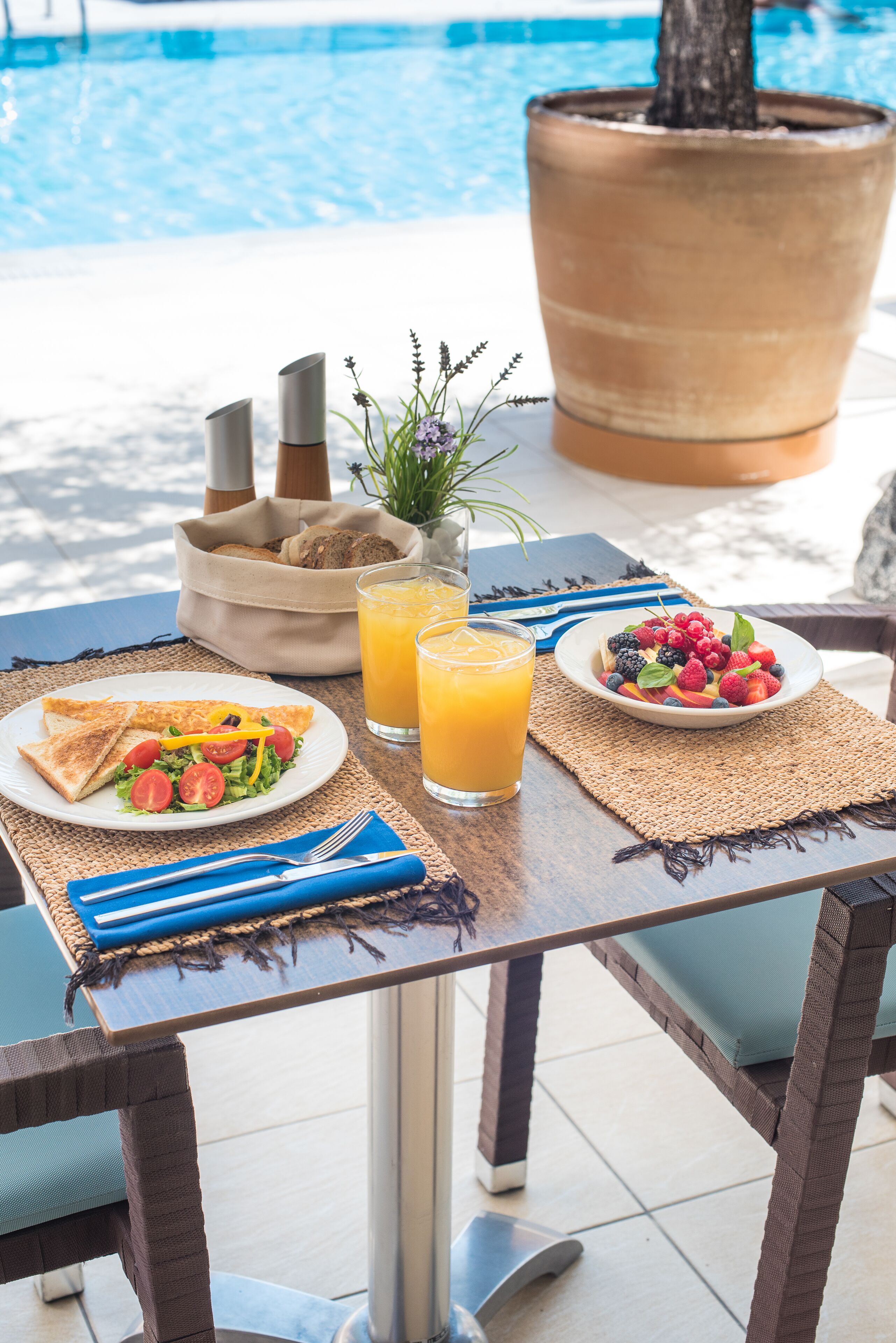A breakfast table with toast, salad, fruit, and juice by a poolside.