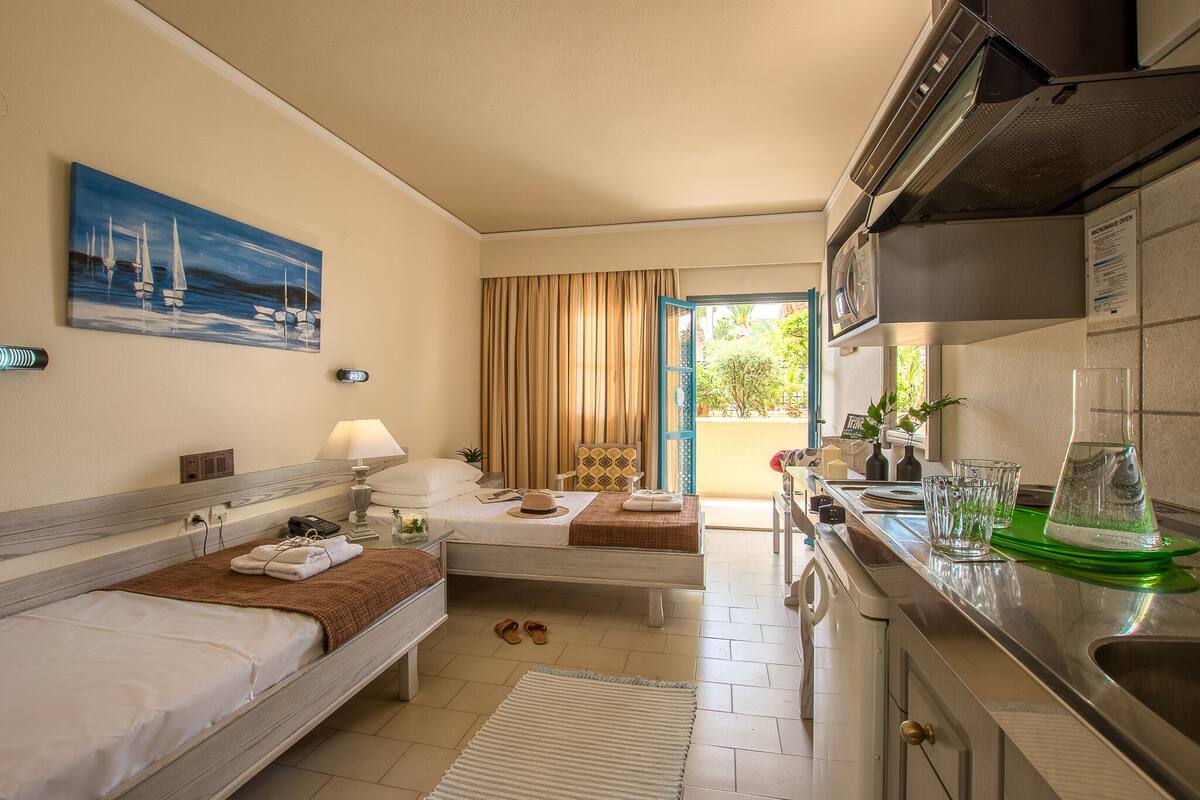 Habitación de hotel con dos camas, kitchenette, un cuadro de veleros y vistas al exterior.