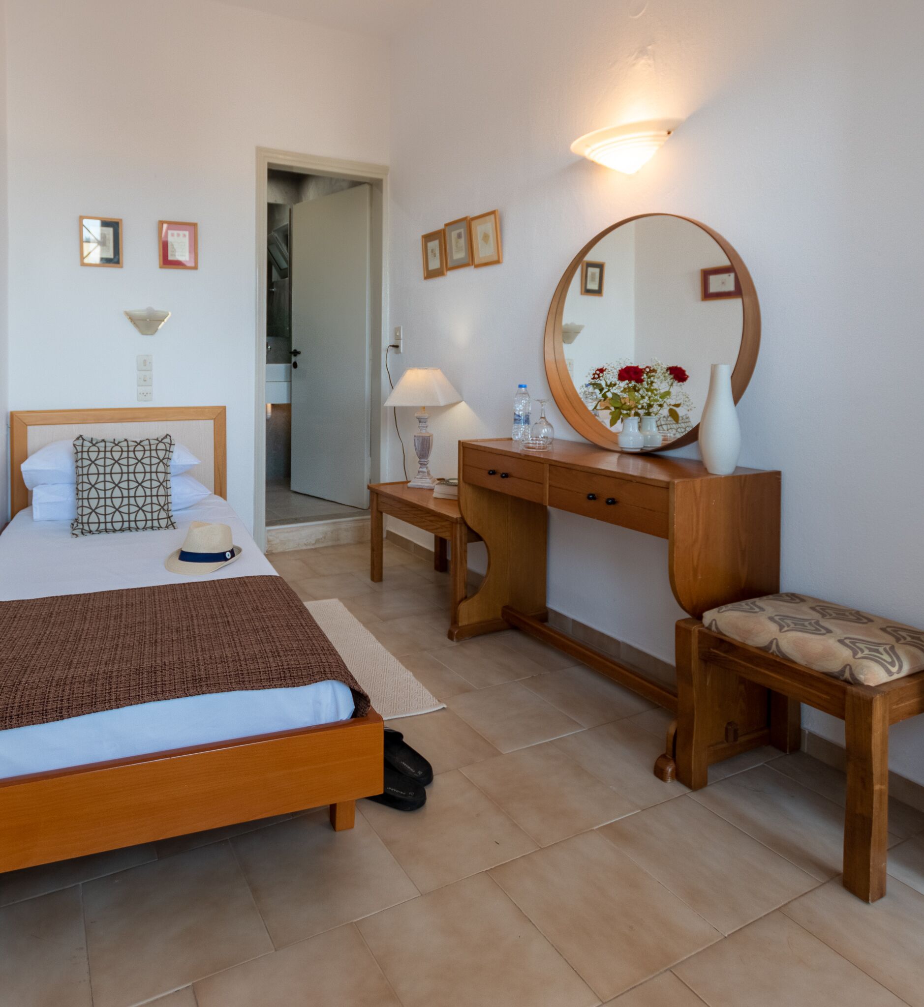 Un dormitorio con cama, mesita de noche, cómoda, espejo y una puerta que da a otra habitación.
