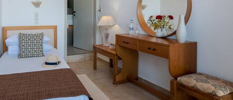 Un dormitorio con cama, mesita de noche, cómoda, espejo y una puerta que da a otra habitación.