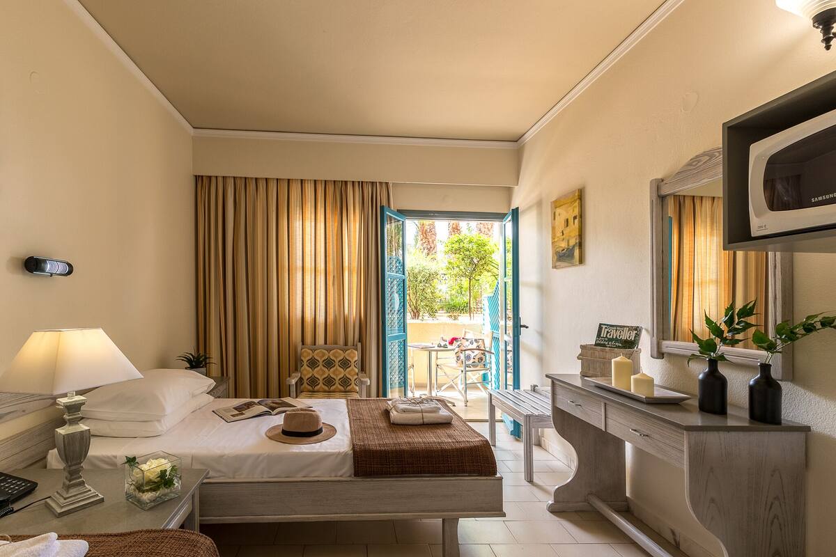 Habitación de hotel con cama, mesita de noche, lámpara y vistas al exterior.