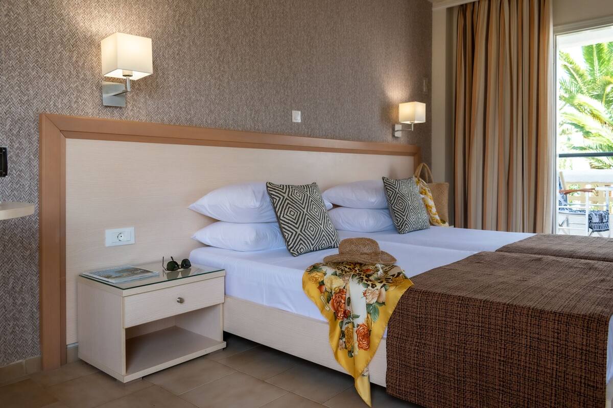 Habitación de hotel con una cama grande, dos mesitas de noche y vistas al exterior.
