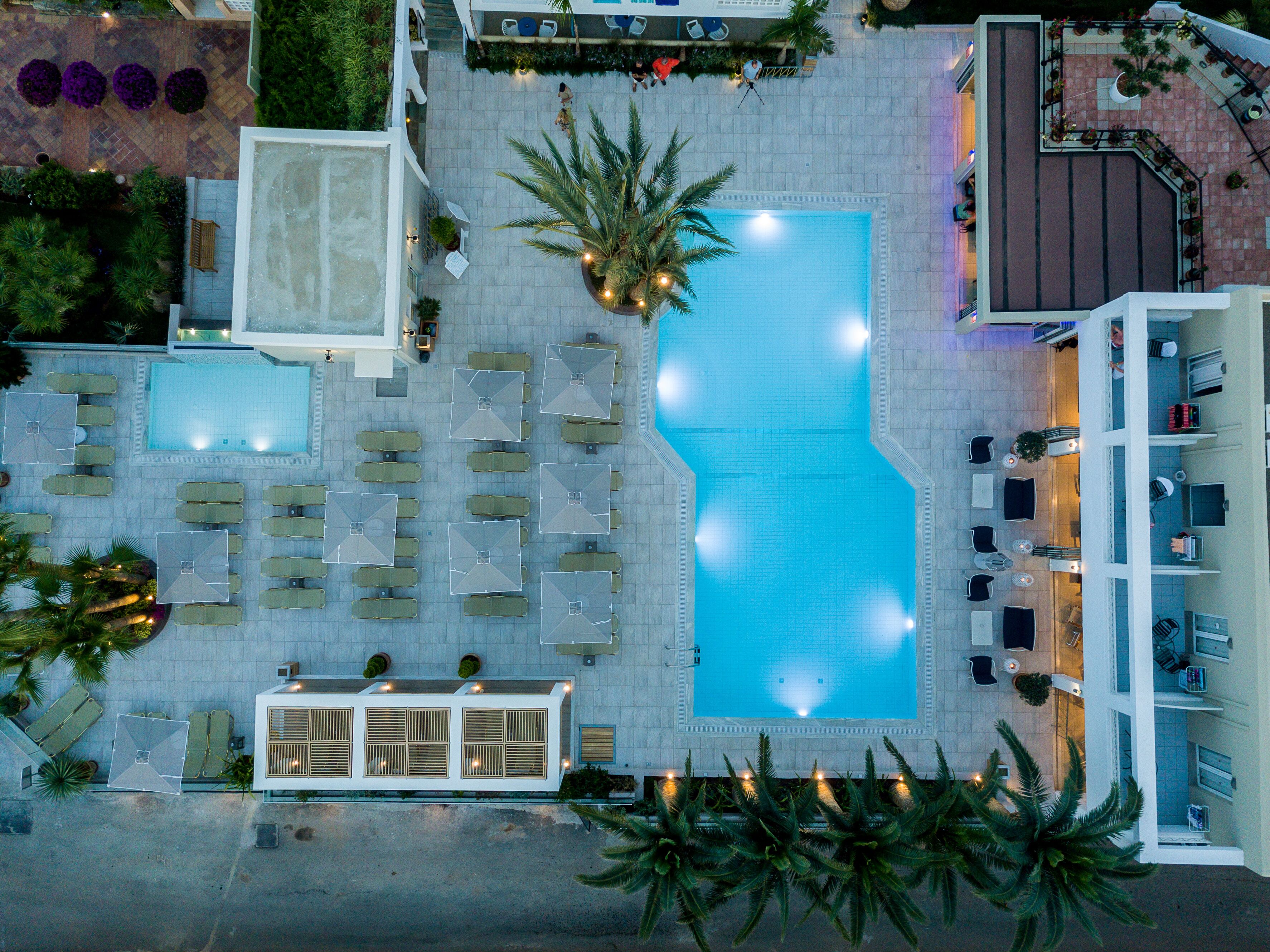 Eine Vogelperspektive eines Hotels mit einem zentralen Schwimmbecken, mehreren Lounges mit Sitzgelegenheiten und einem Gebäude im modernen Stil.