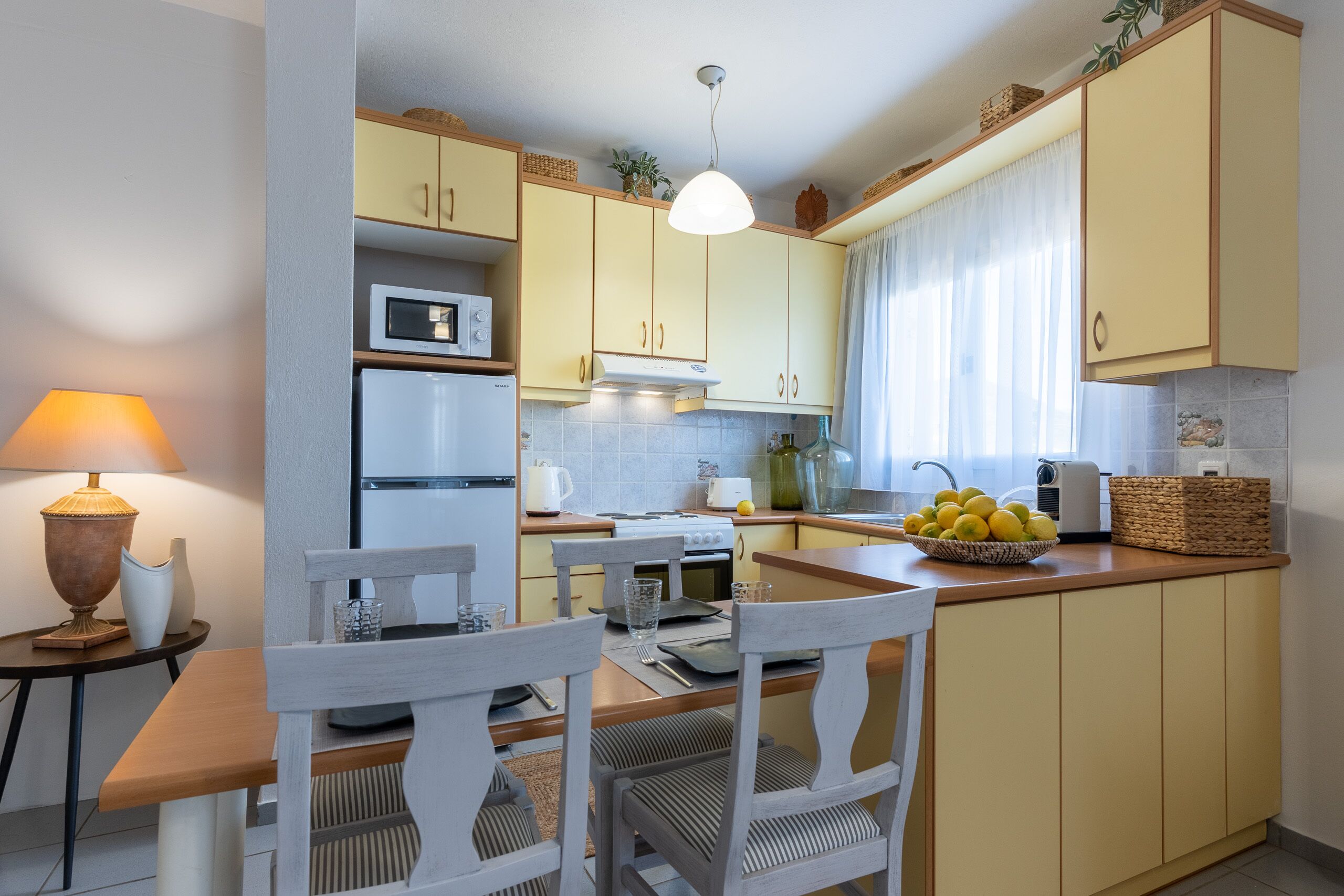 A compact kitchen with yellow cabinets, a white refrigerator, a microwave, and a dining area with a table and chairs.
