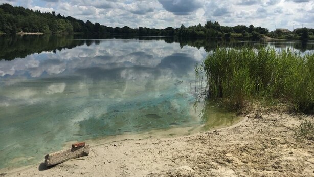 Um lago tranquilo com águas cristalinas refletindo o céu e árvores ao redor.