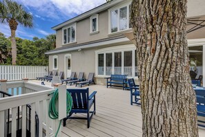 A deck with lounge chairs, a pool, and a tree.
