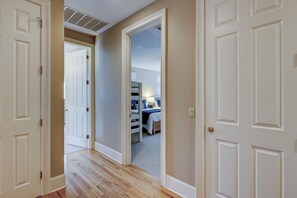 A hallway with wooden flooring leading to a bedroom with a bed and a nightstand.