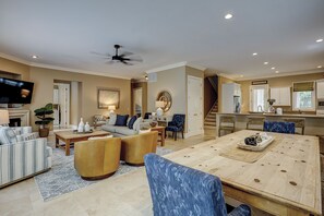 A spacious living room with a large wooden dining table, comfortable seating, a television, and a ceiling fan.