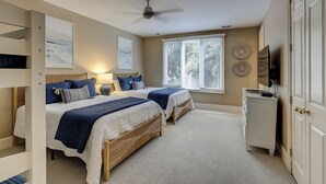 Een slaapkamer met twee bedden, een plafondventilator, een raam met zonwering en een televisie op een kast.