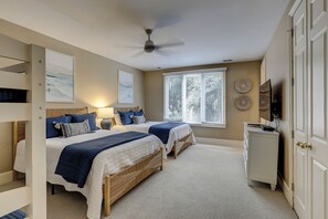 Ein Schlafzimmer mit zwei Betten, einem Deckenventilator, einem Fenster mit Jalousien und einem Fernseher auf einem Schrank.