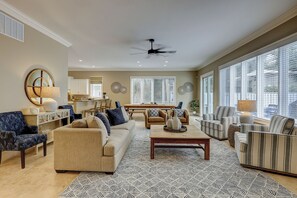 A spacious living room with a beige sofa, striped armchairs, a coffee table, and a ceiling fan.