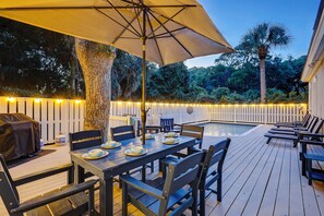 An outdoor deck with a pool, dining table, chairs, and a grill.