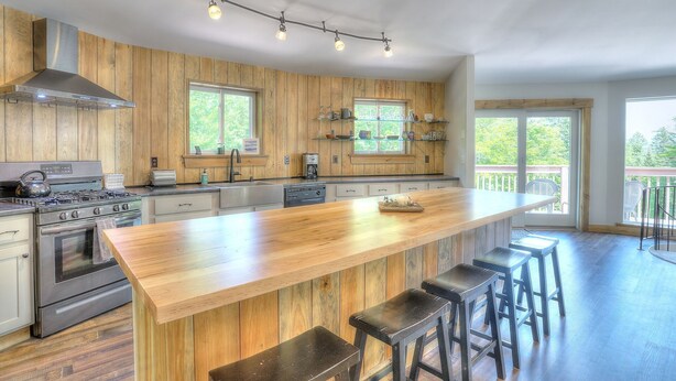 Cocina moderna con paneles de madera, electrodomésticos de acero inoxidable, una isla grande con taburetes de bar y un balcón con vistas.