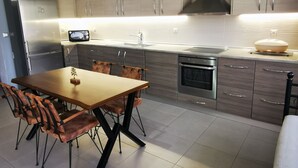 A modern kitchen with a dining table, chairs, a refrigerator, microwave, oven, and a hanging light fixture. - Villa MATA - 600m² with Private Pool and Jacuzzi (Kalithies)