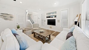 A modern living room with a white sofa, a coffee table, and a TV. There is a staircase in the background leading to another level. - Luxe Destin Miramar Beach Walk to Beach, Private Heated Pool (Destin)