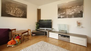 Een moderne woonkamer met een flatscreen televisie, houten meubels en twee grote zwart-wit stadsgezicht schilderijen.