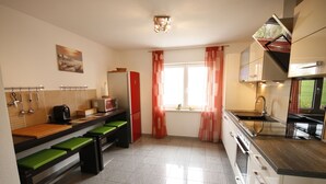 Een moderne keuken met een houten aanrecht, een groene gestoffeerde bank, roestvrijstalen apparatuur en een raam met rode gordijnen.