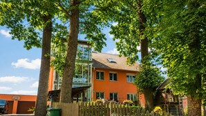 Een woongebouw met een houten omheining, een groene afvalcontainer en een heldere lucht.