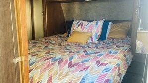 Une chambre à coucher avec un lit recouvert d’une couvre-lit aux motifs géométriques multicolores, une tête de lit en bois et un oreiller marron.