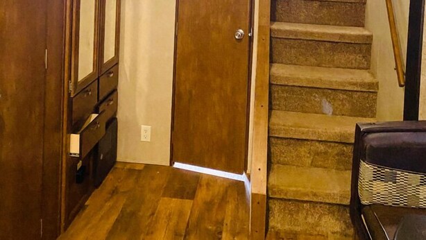 Un escalier en bois, un ventilateur de plafond, une porte en bois et une plateforme recouverte de moquette.