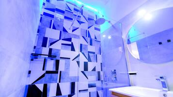 A modern bathroom with a geometric tile backsplash, a glass shower enclosure, and a white sink with a wooden countertop.
