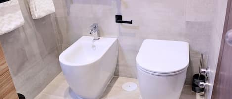 Une salle de bain moderne équipée d’un bidet, de toilettes et d’un porte-serviettes.