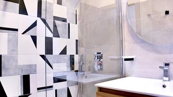 A modern bathroom with a geometric tile backsplash, a glass shower enclosure, and a wooden vanity with a white sink and chrome fixtures.