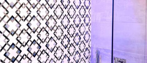 A modern bathroom with a geometric patterned wall, a glass shower enclosure, and a visible showerhead.