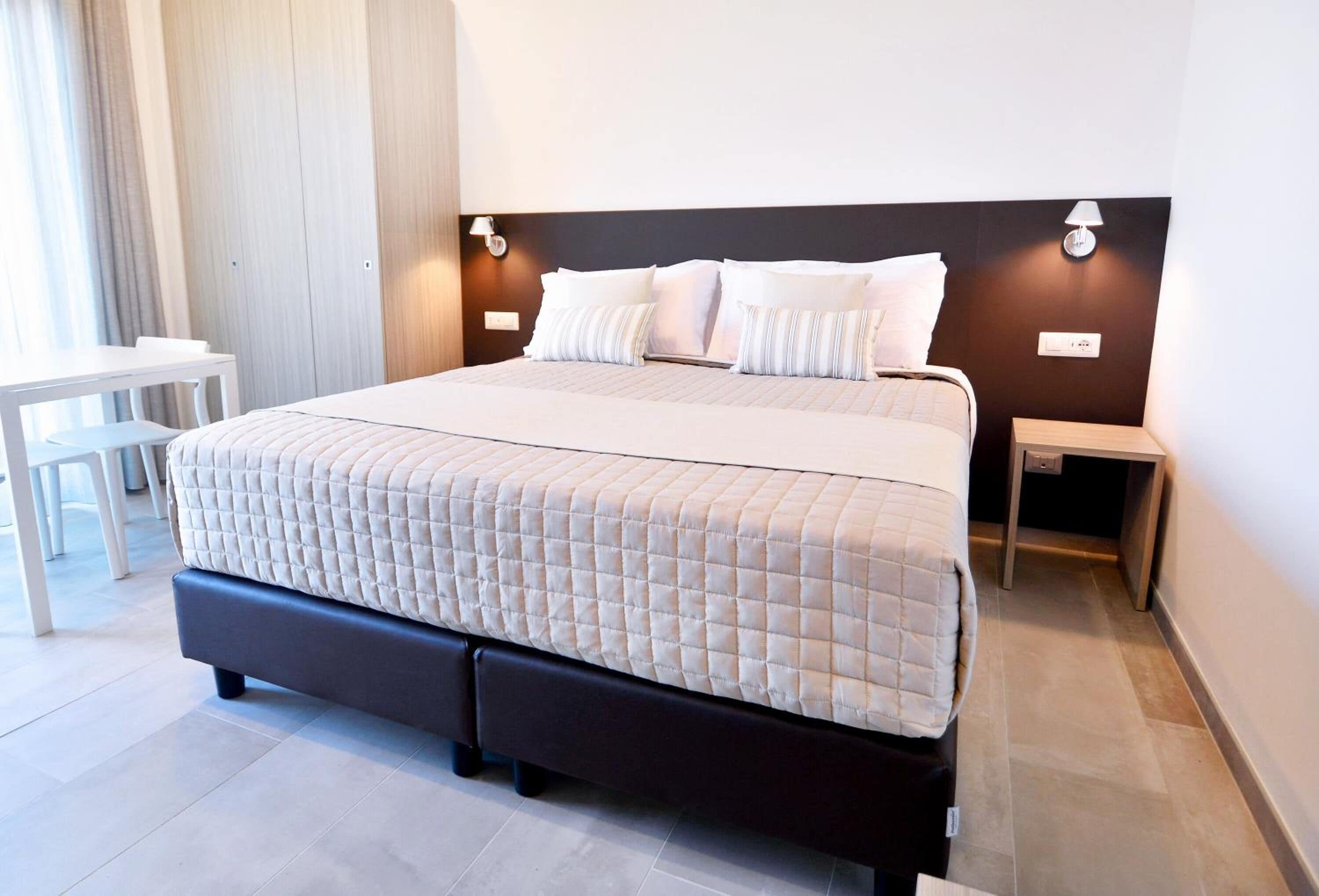 Quarto de hotel moderno com uma cama grande, mesas de cabeceira e uma pequena escrivaninha.