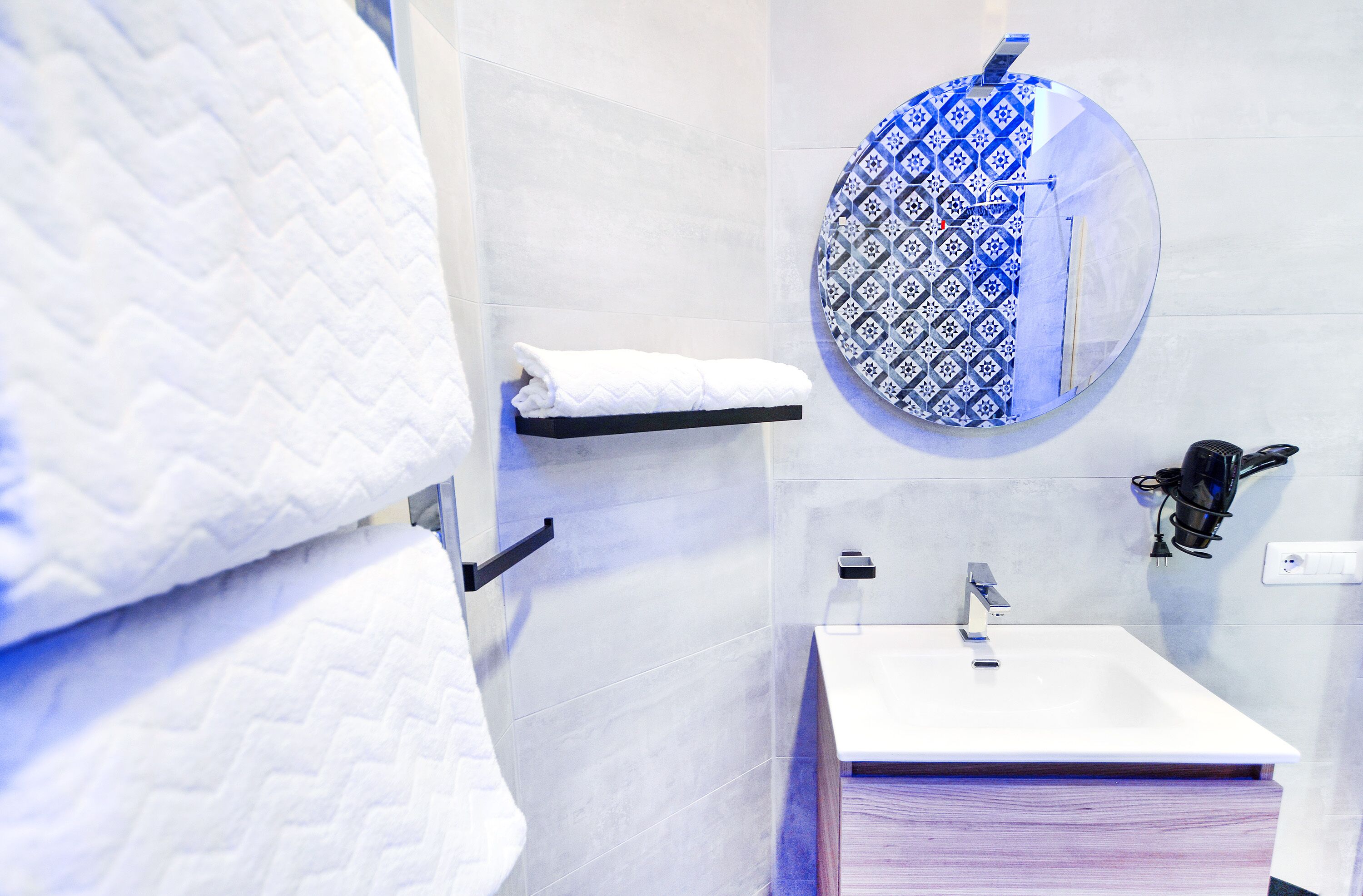 A bathroom with a white sink, a towel rack, and a mirror with a blue patterned frame.