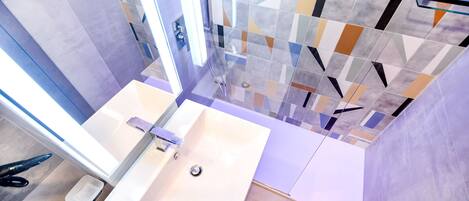 A modern bathroom with a white sink, a glass shower enclosure, and a tiled wall with geometric patterns.