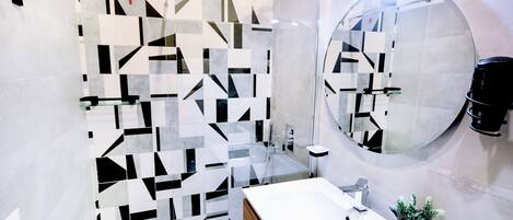 Ein modernes Badezimmer mit einem geometrisch gemusterten Rückspritzschutz, einem großen Spiegel, einem weißen Waschbecken und einem kleinen Topfpflanzen.