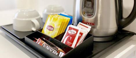A tray with a silver kettle, a white cup, and a black tray containing Lipton tea bags, Eridantia coffee pods, and Nespresso coffee capsules.